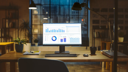 Poster - Shot of a Desktop Computer with Statistics Graph, Chart and Various Data, Showing Company Growth and Success. In the Background Warm Evening Lighting and Open Space Studio with City Window View.