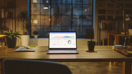 Aufkleber - Shot of a Laptop on a Desk with Statistics Graph, Chart and Various Data, Showing Company Growth and Success. In the Background Warm Evening Lighting and Open Space Studio with City Window View.