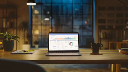 Poster - Shot of a Laptop on a Desk with Statistics Graph, Chart and Various Data, Showing Company Growth and Success. In the Background Warm Evening Lighting and Open Space Studio with City Window View.