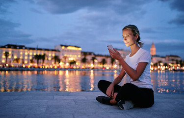 Wall Mural - Young woman using smartphone at city evening lights.