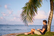 © luengo_ua - Work and vacation. Young man working on laptop computer on the tropical beach under the palm tree.