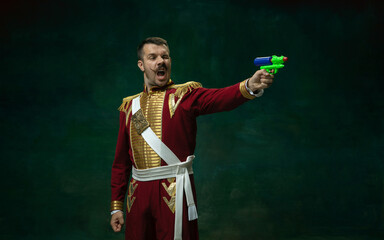 Wall Mural - Shoting. Young man in suit as Nicholas II isolated on dark green background. Retro style, comparison of eras concept. Beautiful male model like historical character, monarch, old-fashioned.