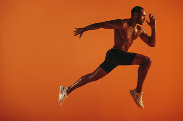 muscular athlete running on orange background