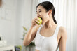 © sunchai - A pretty healthy Asian woman is eating green apple inside her home. Healthy weight loss ideas.