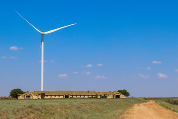 Windmill for electricity generation against the backdrop of the utility room blue sky and road. Renewable electricity generation concept. Green, alternative energy