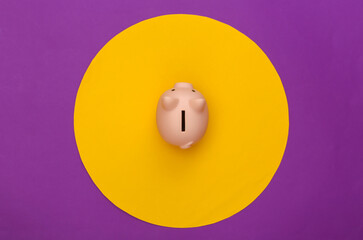 Wall Mural - Piggy bank on purple background with yellow circle. Conceptual studio shot. Minimalism. Top view