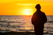 © CrispyMedia - Dark silhouette of a man standing by the sea at golden sunset. Lonely teenager looking a setting sun.