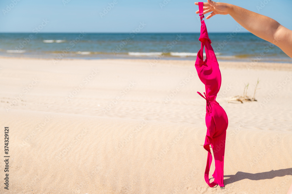 Close up of young woman taking off her bra at nude beach. Concept of sunbathing naked on the