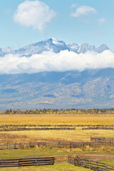 Wall Mural - Beautiful calm rural autumn landscape with yellowed fields against the background of mountain snow-capped peaks with low clouds on a sunny day. Buryatia, Eastern Sayans, Baikal region, Tunka Valley