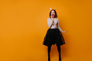 Funny, bright, emotional cheerful girl in a New Year's sweater, fluffy skirt and a hoop on her head jumps on the photo, looks into the camera and shouts happily.