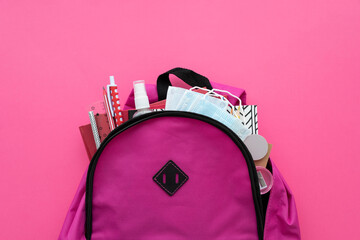 Back to school. New normal with quarantine. Backpack with school supplies and set of hand sanitizers and medical protective masks on pink background. Top view. Copy space