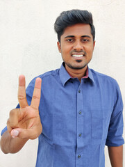 Smiling south indian young man wearing blue shirt pointing up with fingers number two. Isolated on white background.