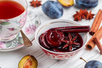 Wall Mural - Delicious homemade plum jam with cinnamon and star anise on a white wooden background. Fresh fruit, spices and cups of tea on the table. Selective focus