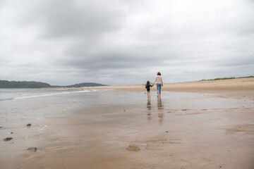 Sticker - Mother and daughter walking down a sandy beach in the summer