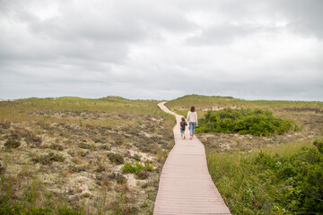 Wall Mural - Mother and daughter walking down a wooden path to the beach