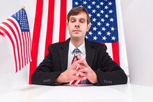 Lobbyist Looks At Camera. Young Man On Background Of American Flag. Concept - Man Works As A Lobbyist In America. Lobbying Business. Promotion Of Interns. Lobbying Interests In The United States