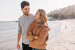 © Look! - Pleasant young man embracing girlfriend on nature background. Outdoor photo of pleased blonde girl posing at sea with husband.