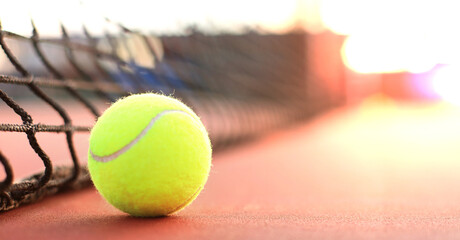 Bright greenish yellow tennis ball on clay court.