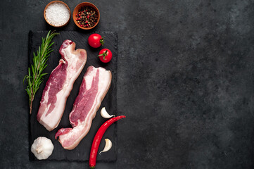 raw pork breast with spices on a slate board on a stone background with copy space for your text