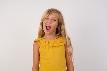 Wall Mural - Little blond girl wearing yellow dress over white background winking looking at the camera with sexy expression, cheerful and happy face.