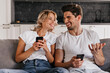 © Look! - Laughing young man talking with wife on sofa. Pretty girl chilling on couch and texting message.