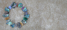 Crystal And Abalone Shell Circle Website Header - Tumbled Stones And Slices Of Abalone Shell Neatly Arranged In A Circle Border Against Handmade Fibrous Beige Paper With Copy Space On Right 
