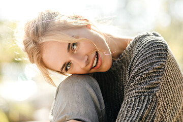 Wall Mural - Attractive blonde green-eyed woman in gray outfit put her head on her knees and posing on street