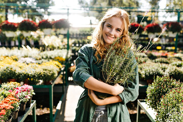 Wall Mural - Girl in khaki cotton clothes smiles warmly and looks into camera with joy. Feminine model loves lavender and holds bush in hands