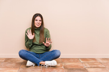 Wall Mural - Young caucasian woman sitting on the floor isolated rejecting someone showing a gesture of disgust.