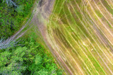 Fototapeta Las - Aerial landscape with harvested field, dirt road and forest