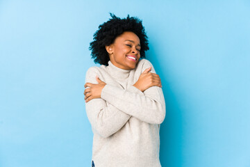 Wall Mural - Middle aged african american woman against a blue background isolated hugs, smiling carefree and happy.