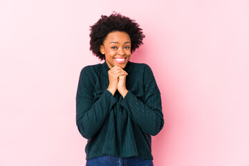 Wall Mural - Middle aged african american woman against a pink background isolated keeps hands under chin, is looking happily aside.