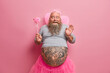 © wayhome.studio  - Photo of comic male fairy with thick beard and fat tattooed belly, giggles positively, wears crown on head, holds magic wand, organises real holiday for children, poses against rosy background