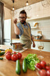 © Svitlana - Italian man adding pepper, spice to the soup while preparing a meal in the kitchen. Cooking at home, Italian cuisine