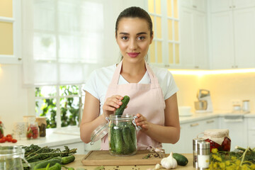 Canvas Print - Woman putting cucumber into pickling jar at table in kitchen