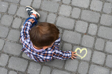 Yellow Heart Drawn With Chalk On Asphalt And A Little Boy Next To These Drawing.