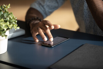 Close up male hands touching phone screen, African American businessman sitting at modern work desk, browsing mobile device apps, using daily planner, checking email, chatting in social network