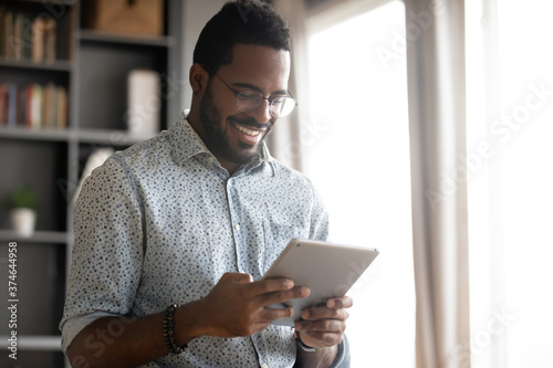 Photographie Smiling African American man wearing glasses holding computer tablet, looking at