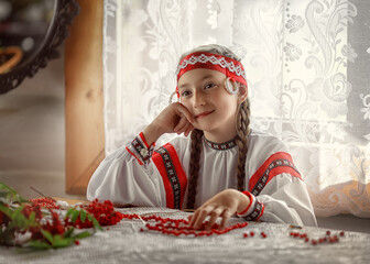 Wall Mural - Beautiful Russian girl smiles sitting at the table. Portrait of a girl in red Rowan berry beads. Russian folk dress.