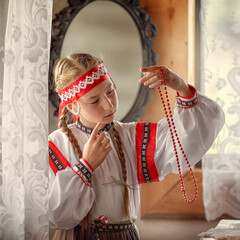 Wall Mural - A beautiful girl in a folk costume looks at the Rowan berry beads. The young girl thought about something. Traditional Russian costume.