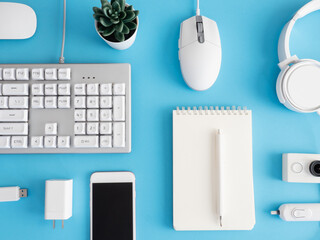 Poster - top view of office desk table with notebook, plastic plant, smartphone and keyboard on blue table background, graphic designer, Creative Designer concept.