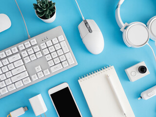 Poster - top view of office desk table with notebook, plastic plant, smartphone and keyboard on blue table background, graphic designer, Creative Designer concept.