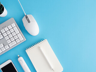 top view of office desk table with notebook, plastic plant, smartphone and keyboard on blue table background, graphic designer, Creative Designer concept.