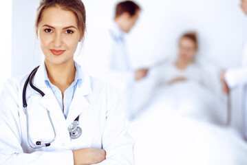 Wall Mural - Female doctor smiling on the background with patient in the bed and two doctors