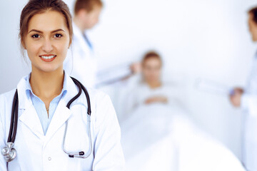 Wall Mural - Female doctor smiling on the background with patient in the bed and two doctors