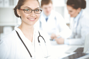 Happy smiling woman-doctor sitting and looking at camera at meeting with medical staff . Medicine concept