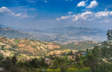 Fototapeta Do pokoju - The eastern part of the Kathmandu valley, on a sunny day, with the hills and foothills of the Himalayas, terraces with agricultural crops, against the backdrop of a blue sky and clouds.