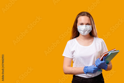 Quarantine class. Pandemic hygiene. Happy woman in protective face mask gloves with books isolated on orange copy space ready for class. Coronavirus pandemic. New normal. Safety measures.