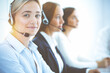 © rogerphoto - Cheerful smiling business woman with headphones consulting clients. Group of diverse phone operators at work in sunny office.Call center and business people concept