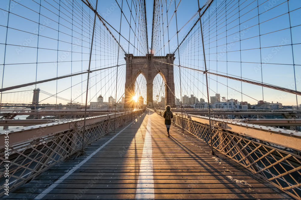 Woman walking across the Brooklyn Bridge at sunrise, New York City, USA - obrazy, fototapety, plakaty 